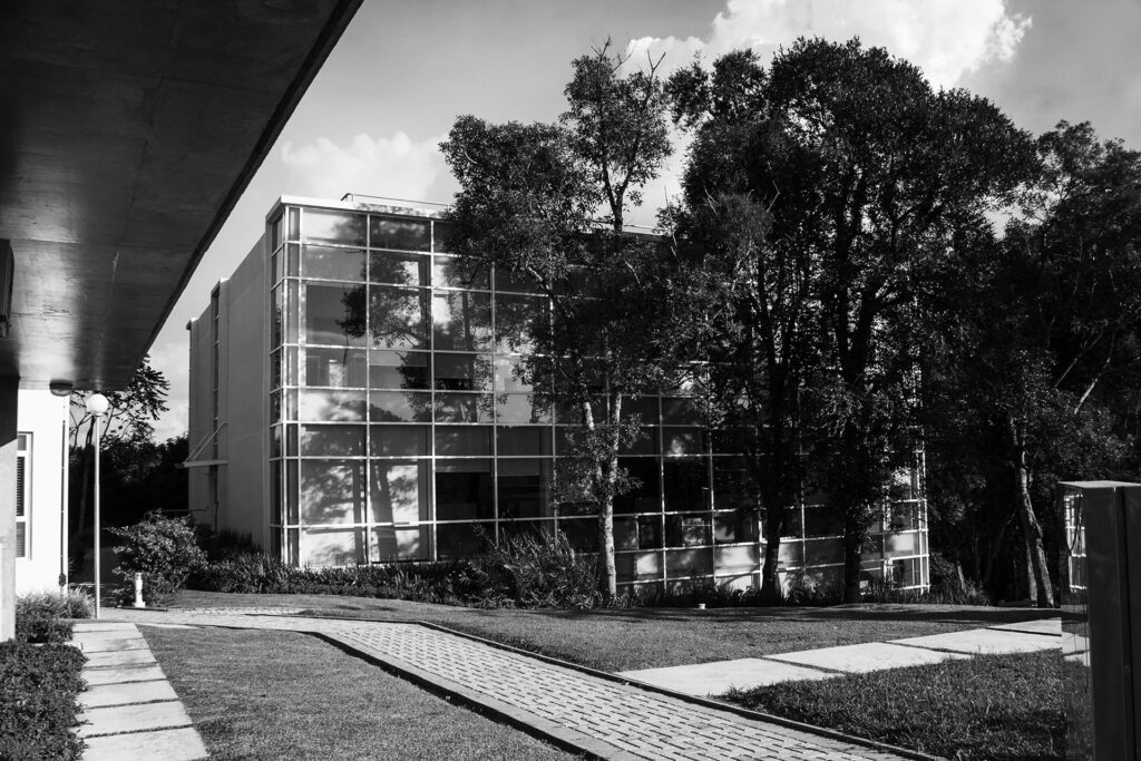 Uma foto em preto e branco de um prédio baixo com fachada de vidro com árvores na frente.